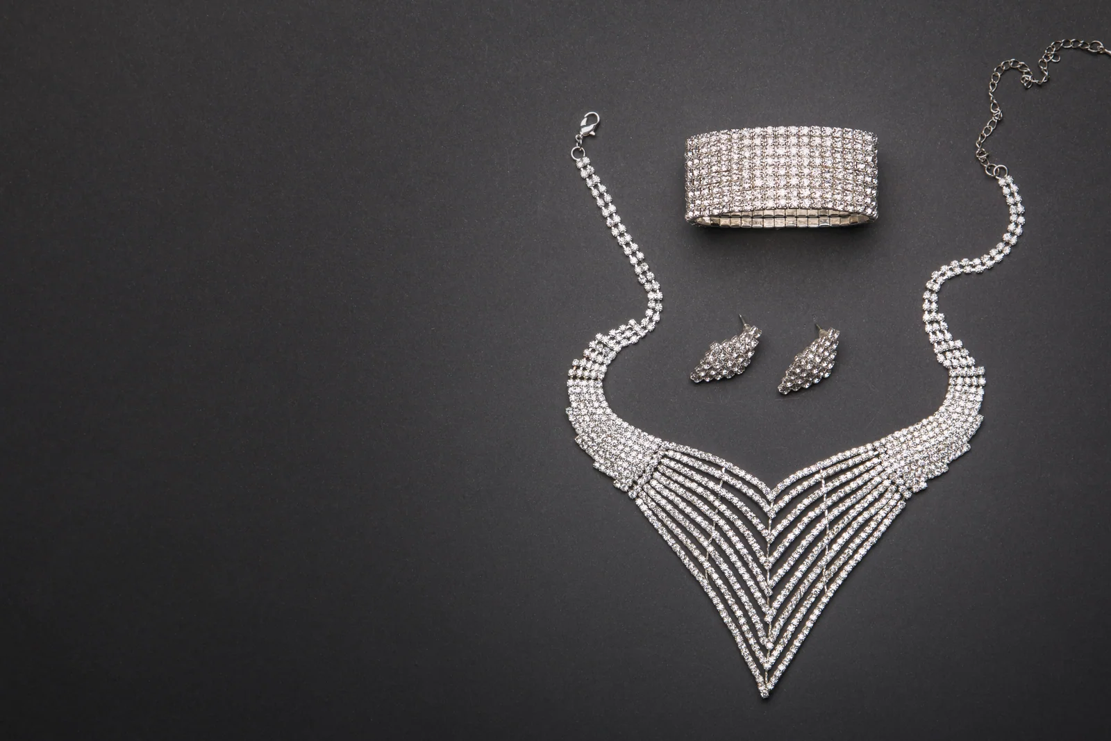 Silbernes Schmuckset mit Halskette, Ohrringen und Armband auf dunklem Hintergrund